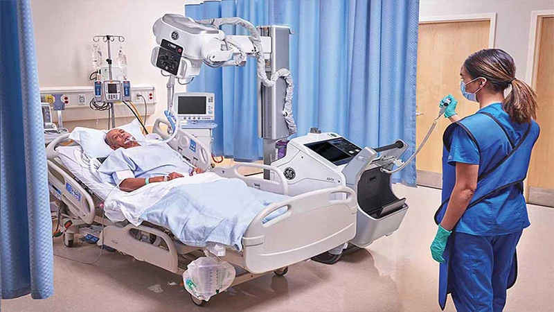 A busy trauma bay scene with a technologist performing a portable chest X-ray on a patient.